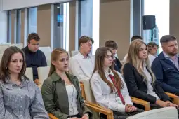 Grupa młodych ludzi i dorosłych siedzących w sali konferencyjnej.
