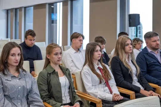 Grupa młodych ludzi i dorosłych siedzących w sali konferencyjnej.