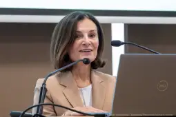 Kobieta w beżowym żakiecie przemawia do mikrofonu, obok laptop.