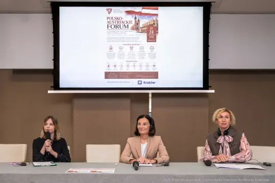 Trzy kobiety siedzą przy stole, prezentacja na ekranie dotyczy Polsko-Austriackiego Forum.