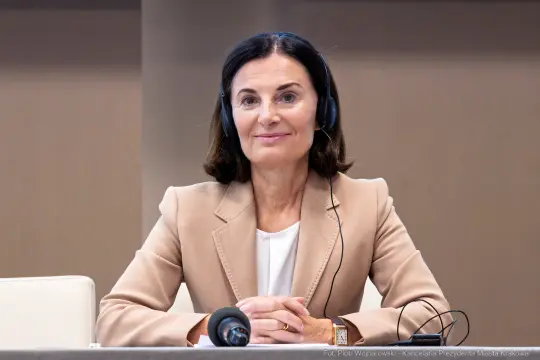 Kobieta w beżowym żakiecie z słuchawkami, siedząca przy stole.