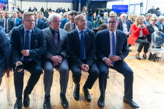 Czterech mężczyzn w garniturach siedzących na widowni podczas wydarzenia.