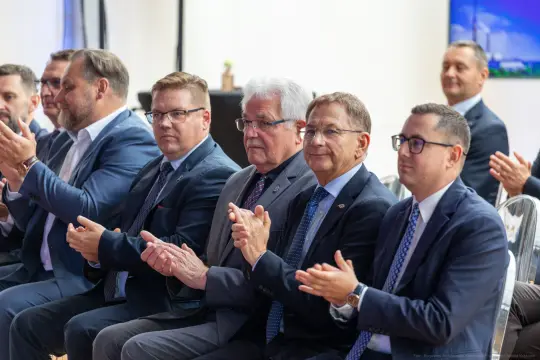 Grupa mężczyzn w garniturach, klaskających podczas wydarzenia.
