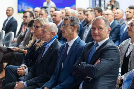 Grupa mężczyzn w garniturach siedzących na wydarzeniu, zwróconych w stronę prelegenta.