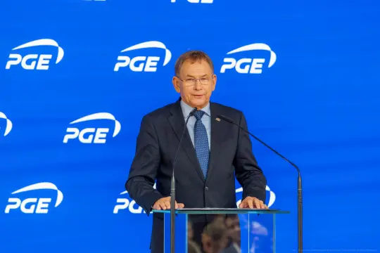 Mężczyzna w garniturze przemawia przy mównicy, w tle logo PGE.