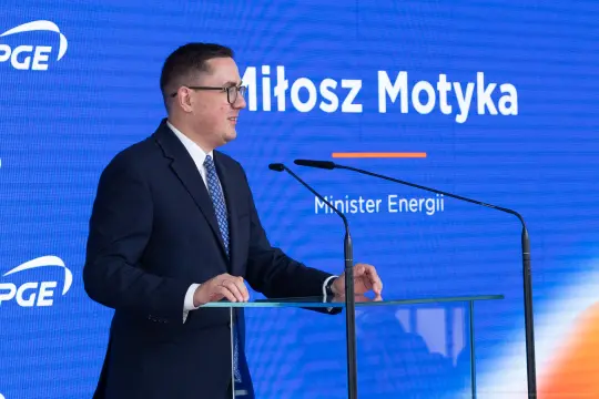 Mężczyzna w garniturze przemawia przy mównicy, w tle logo PGE i napis "Miłosz Motyka, Minister Energii".