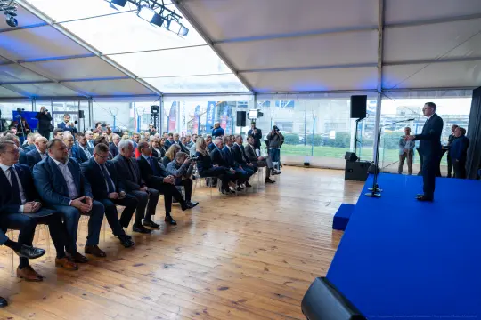 Spotkanie w namiocie z mówcą na scenie i publicznością siedzącą na krzesłach.