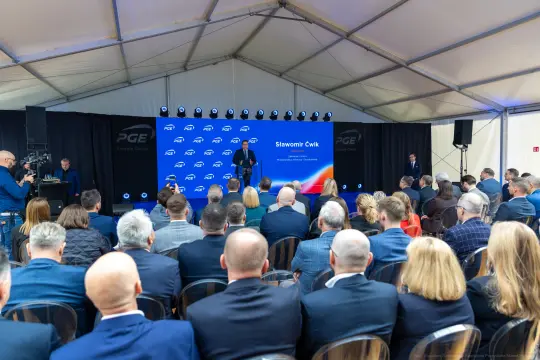 Konferencja z udziałem wielu osób, na scenie mężczyzna przemawiający do publiczności.