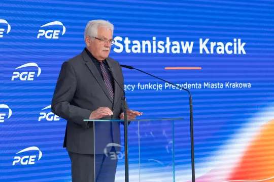 Mężczyzna w garniturze przemawia przy mównicy z logo PGE w tle.