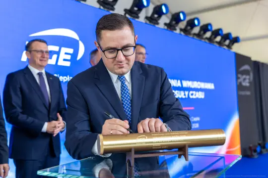 Mężczyzna podpisuje złotą tubę podczas ceremonii związanej z inwestycją PGE.