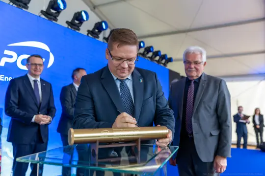Mężczyzna podpisuje złotą tubę podczas ceremonii związanej z projektem energetycznym.
