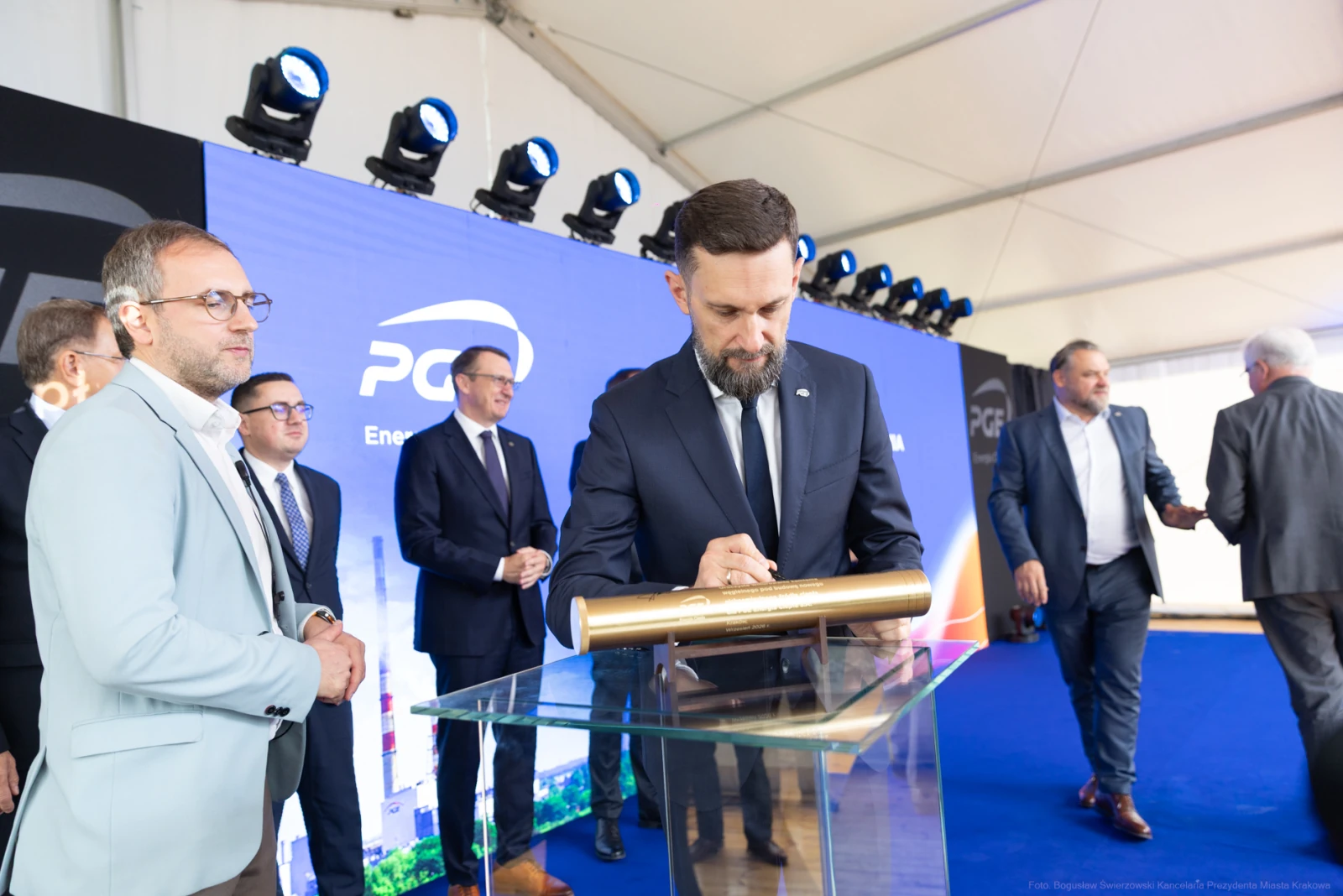 Mężczyzna podpisuje dokument na tle logo firmy energetycznej. Wokół inni uczestnicy wydarzenia.  Autor: Bogusław Świerzowski