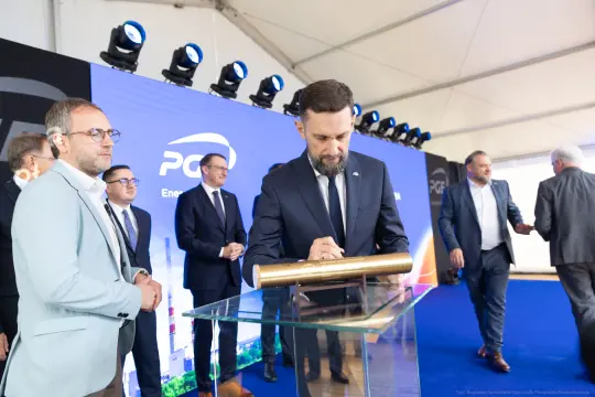 Mężczyzna podpisuje dokument na tle logo firmy energetycznej. Wokół inni uczestnicy wydarzenia.