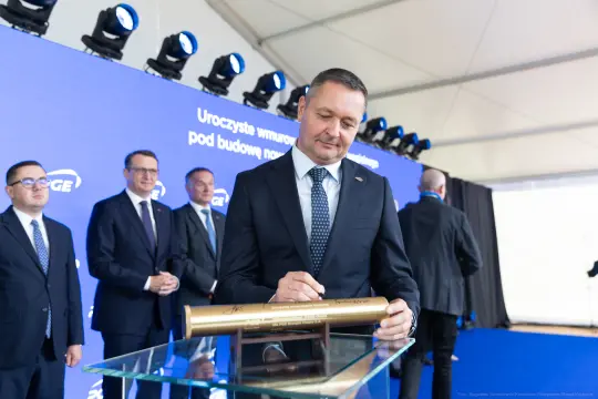 Mężczyzna podpisujący złotą tubę podczas uroczystości związanej z budową.