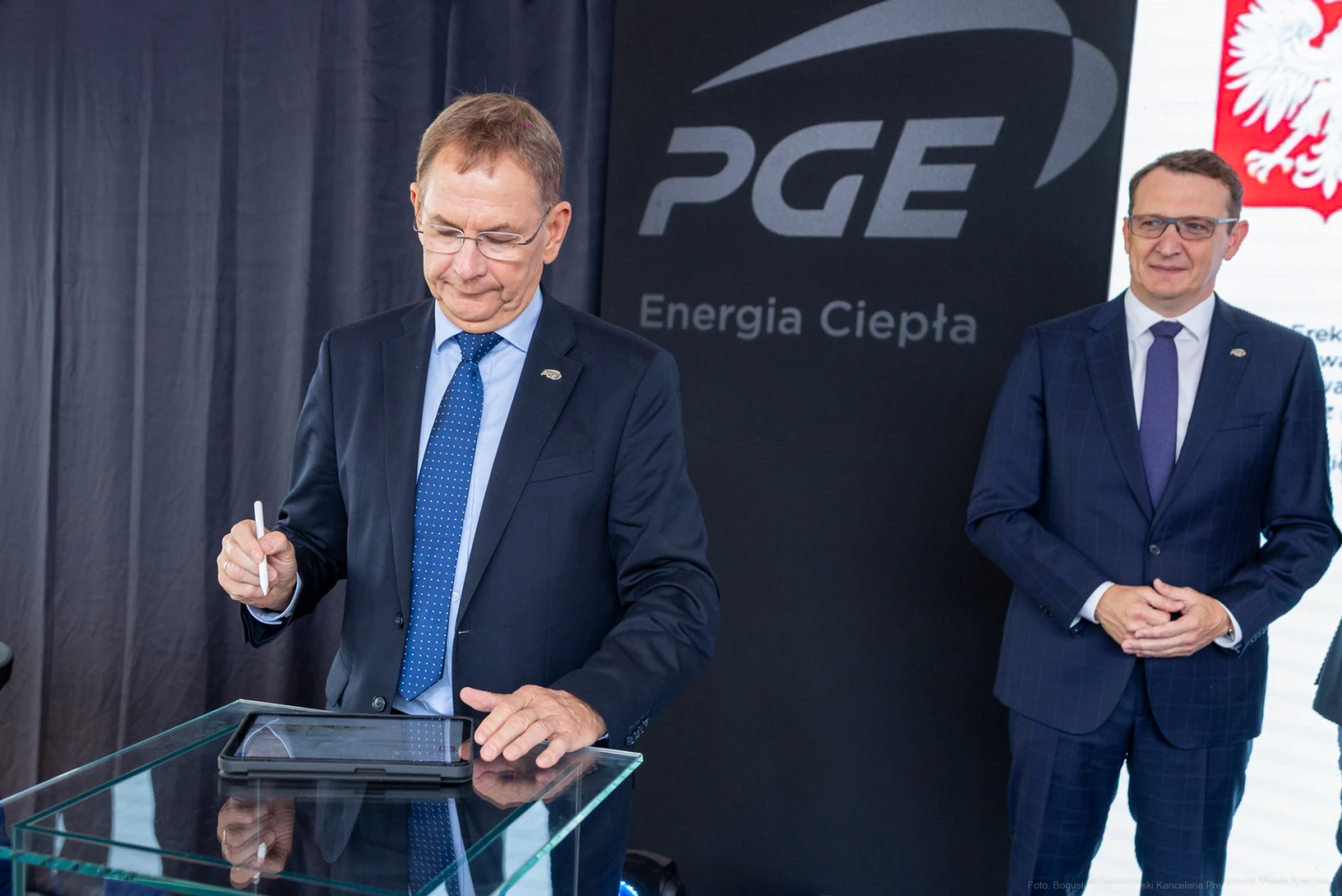 Mężczyzna podpisuje dokument na tablecie, obok stoi drugi mężczyzna w garniturze.  Autor: Bogusław Świerzowski