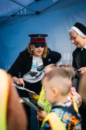 Kobieta w mundurze i zakonnica rozmawiają z dziećmi przy stoisku.