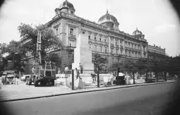 Budowa pomnika przed historycznym budynkiem z kopułami. Pracownicy i maszyny na placu budowy.