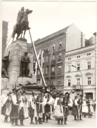 Parada z uczestnikami w tradycyjnych strojach ludowych przed pomnikiem konnym.