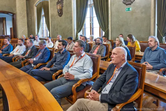 Grupa osób siedzących w sali konferencyjnej, uczestniczących w spotkaniu.