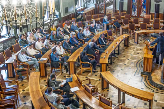Spotkanie w sali obrad z uczestnikami siedzącymi przy okrągłych stołach.