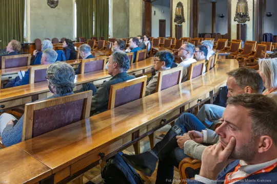 Grupa ludzi siedzących w sali konferencyjnej, skupionych na prezentacji.