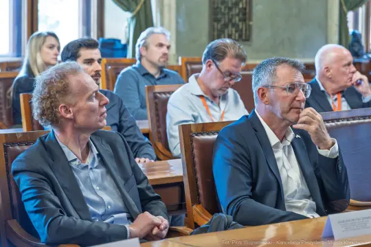 Grupa osób siedzących przy stole, skupionych na dyskusji.