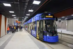 Nowoczesny niebieski tramwaj na stacji, pasażerowie czekają na odjazd.