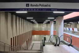 Rondo Polsad 01, nowoczesne wnętrze stacji z ruchomymi schodami i oznaczeniami kierunkowymi.
