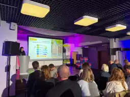Prezentacja na konferencji z widownią, na ekranie slajd z informacjami o turystyce.