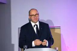 Mężczyzna w okularach prezentuje na konferencji, trzymając w ręku pilot do slajdów.