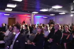 Grupa ludzi uczestniczących w konferencji, z różnorodnymi reakcjami na prezentację.