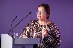 Kobieta w okularach wygłasza przemówienie przy mównicy.