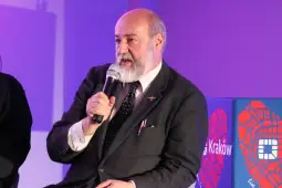 Mężczyzna z brodą trzyma mikrofon, prowadząc dyskusję na wydarzeniu w Krakowie.