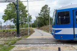 Tramwaj przejeżdżający obok ścieżki rowerowej i zieleni.