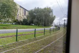 Widok na torowisko tramwajowe, zieleń i budynki w tle.