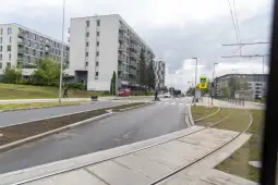 Nowoczesne budynki mieszkalne przy ulicy z torami tramwajowymi i przejściem dla pieszych.