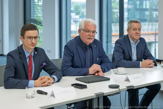 Trzech mężczyzn siedzących przy stole, prowadzących dyskusję w nowoczesnym biurze.