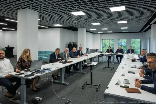 Spotkanie w sali konferencyjnej z uczestnikami przy stole i prezentacją na laptopie.