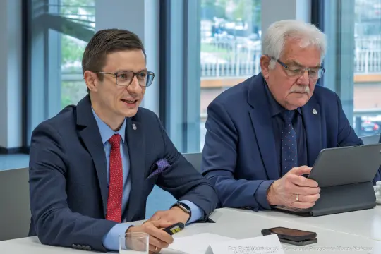 Dwóch mężczyzn w garniturach podczas spotkania, jeden z nich trzyma tablet.