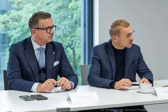 Dwóch mężczyzn w garniturach siedzi przy stole, rozmawiając podczas spotkania.