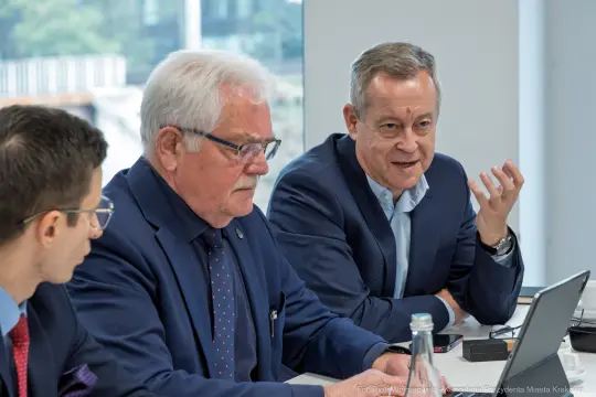 Trzech mężczyzn w garniturach podczas spotkania przy stole.