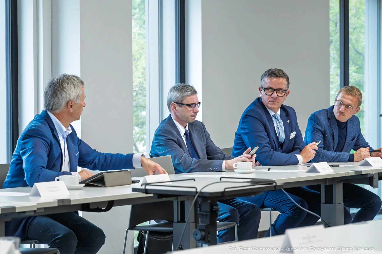 Czterech mężczyzn w garniturach dyskutuje przy stole w nowoczesnym biurze.  Autor: Piotr Wojnarowski