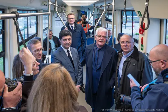 Grupa osób w tramwaju, rozmawiających i uśmiechających się.