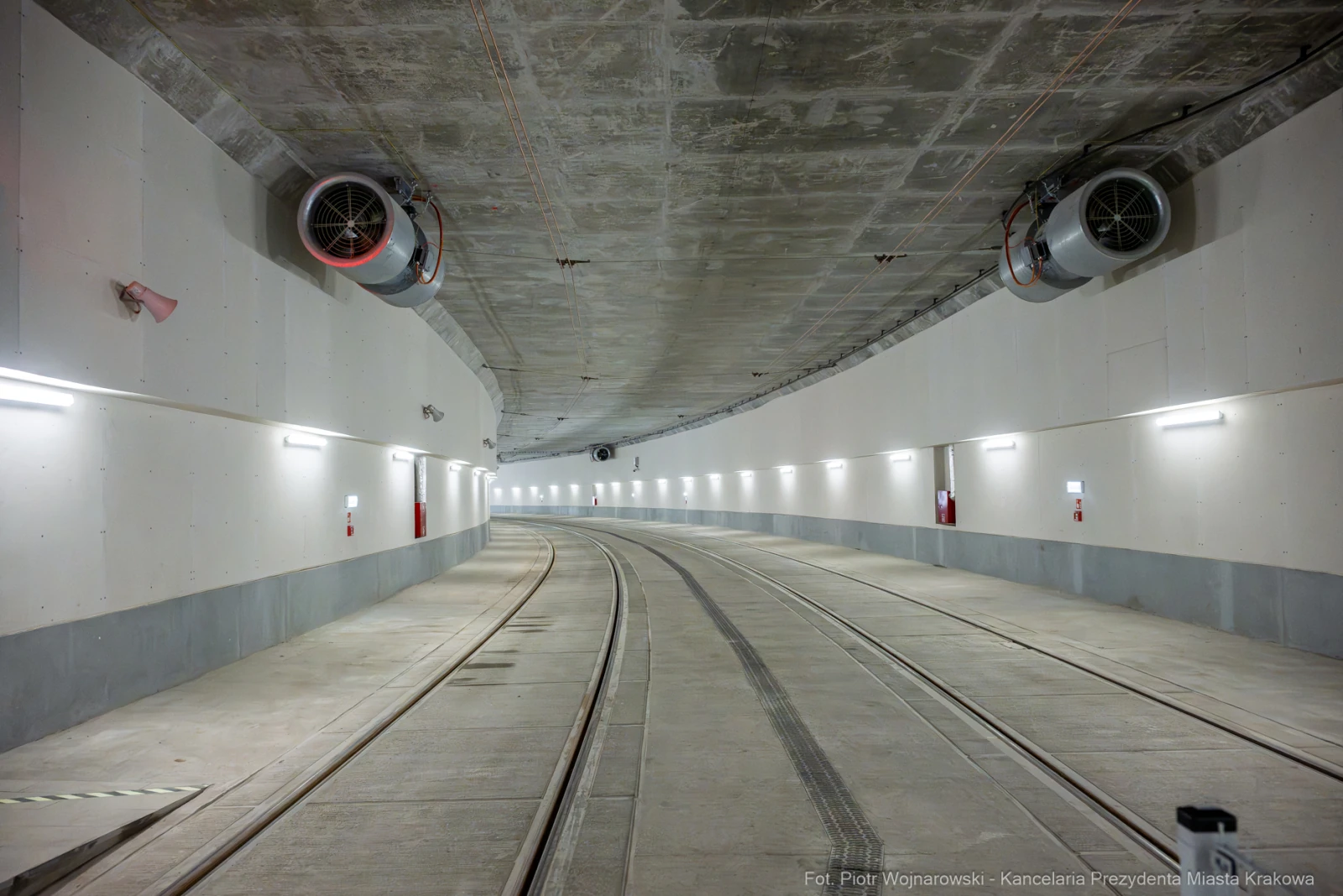 Tunel z zakrętem, oświetlony, z widocznymi wentylatorami i torami tramwajowymi.  Autor: Piotr Wojnarowski