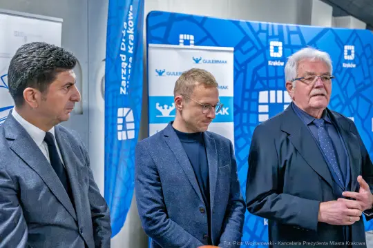 Trzech mężczyzn w garniturach podczas konferencji prasowej w Krakowie.