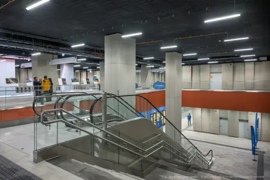 Nowoczesne wnętrze stacji metra z ruchomymi schodami i pasażerami.