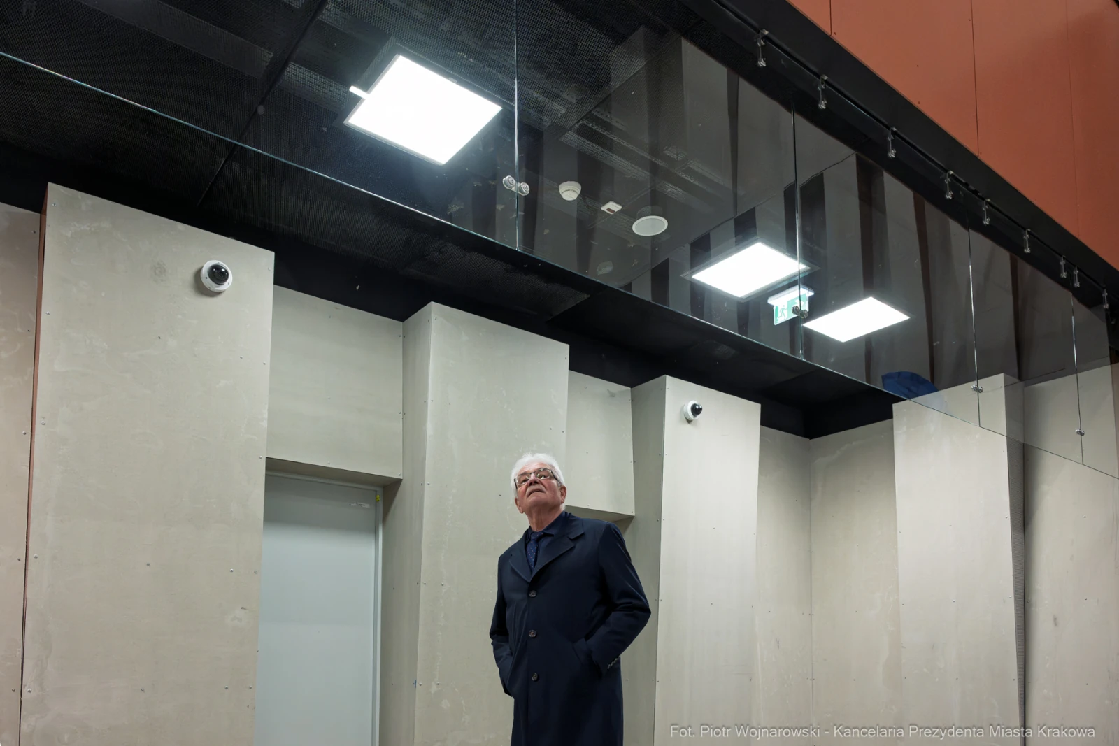 Mężczyzna w płaszczu stoi w nowoczesnym wnętrzu z betonowymi ścianami i sufitami.  Autor: Piotr Wojnarowski
