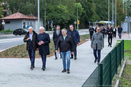 Grupa mężczyzn spacerujących po chodniku w miejskim otoczeniu.