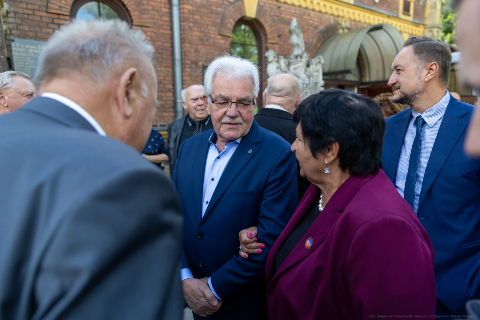 Grupa osób rozmawia na tle budynku, wśród nich mężczyzna w okularach i kobieta w fioletowej marynarce.  Autor: Bogusław Świerzowski