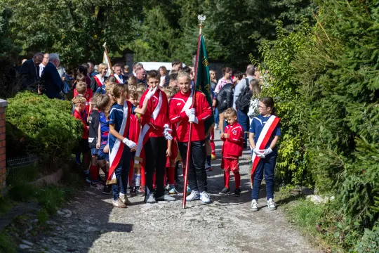 Grupa dzieci w strojach sportowych z flagami, idąca w procesji.